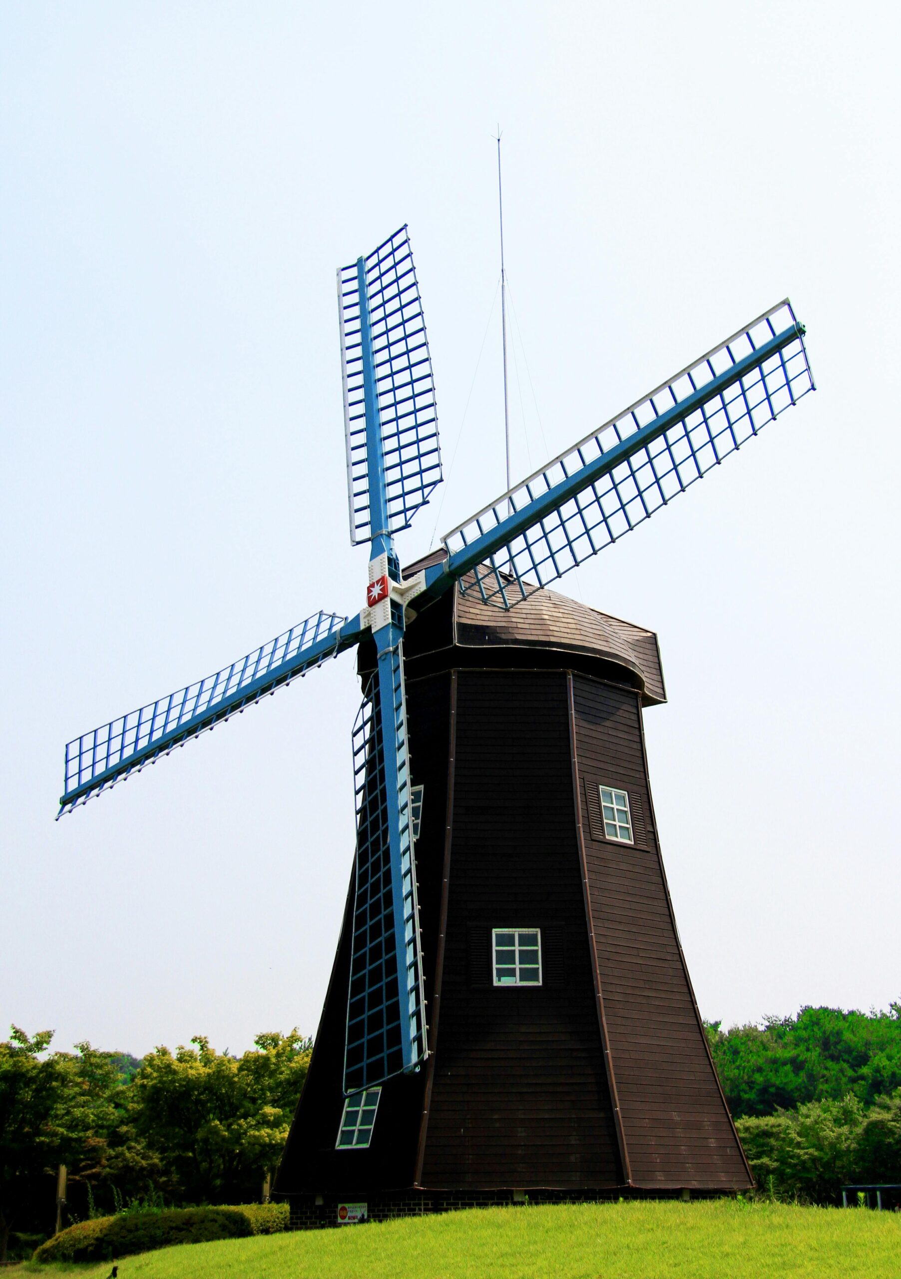 Charming wooden windmill against a bright sky, surrounded by lush greenery.